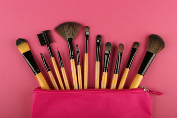 set of makeup brushes in a pink cosmetic bag top view on pink background. concept of make up artist.