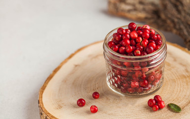 Fresh ripe cranberries in a transparent glass jar on a wooden stand. Autumn, useful berries....