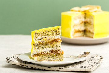 Layered piece of cake with poppy seeds and yellow cream on a white plate for a holiday, light green background, horizontal format.
