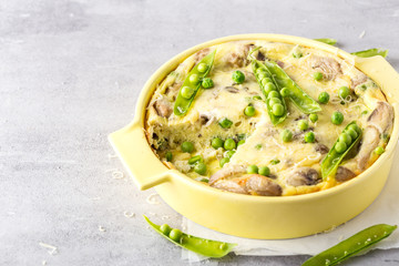 Frittata with, green peas, cheese and champignons in yellow form for baking on light grey background. Horizontal format.