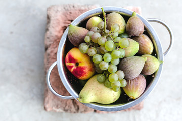 Composition with ripe fresh figs, grape,pear and nectarines in metal bowl on grey background. Healthy sweet dessert, no calories. Close up, top view, copy space for your text