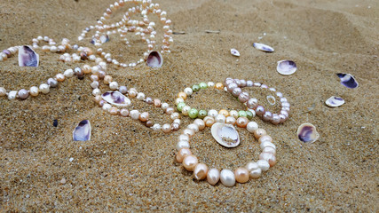 Natural, iridescent pearl jewelry is scattered across the sand on a deserted beach. 