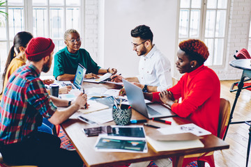 Creative male and female coworkers sitting at cooperation table and discussing education information during time for together e learning, youthful hipsters communicate about business startup project