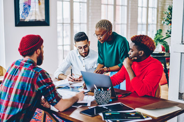 Group of young hipster IT professionals discussing report information during co brainstorming in modern apartment with wifi connection for developing, diverse students preparing to program test