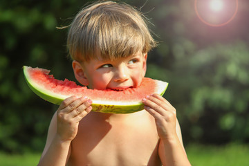 Ein kleiner Junge isst eine Wassermelone im Garten