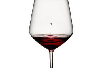 Naklejka na ściany i meble Close-up of a drop of red wine falling into the glass on a white background. Waves are formed in the red wine