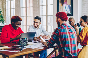 Crew of diverse colleagues enjoying positive discussion during brainstorming at meeting table making plans for successful startup, happy creative designers communicating about project share ideas