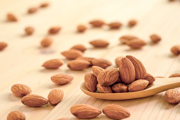 Closeup of brown fresh almonds seed in wooden spoon on table.