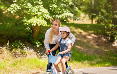 Mom Teaching Little Daughter To Cycle Standing In City Park