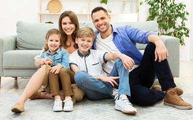 Parents And Two Kids Sitting Near Sofa In Living Room