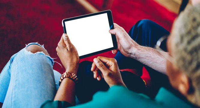 Cropped image of man and woman holding touch pad with mock up screen checking web media during free time at home, back view of hipster guys using app for online booking spending time at apartment