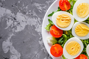 salad with boiled chicken eggs and cherry tomatoes on a stone background