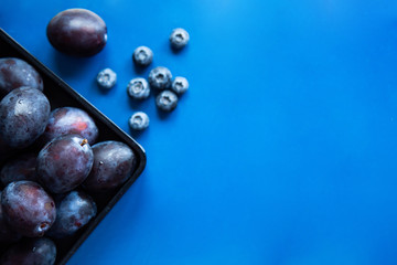 Plums in a black plate on a blue background. Vegetarianism concept with place for text. top view 