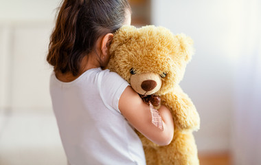 Unrecognizable Kid Girl Embracing Teddy Bear Toy Standing Alone Indoor