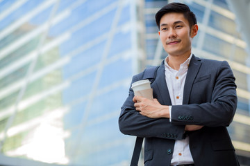 A young confident businessman crossing his arms while hold a cup of coffe on left hand.