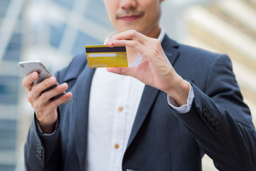 A young confident businessman use credit card to purchase some items by smartphone in the city.