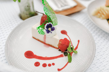 Piece of cheesecake with fresh strawberries and, decorated with flower and jam on white plate. Delicious homemade dessert