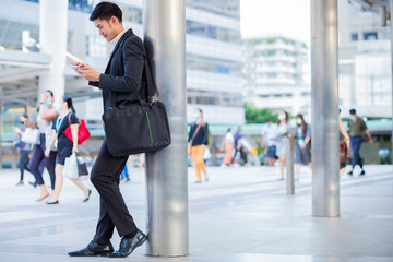 Obraz premium Businessman who wear white shirt leaning on the pole in the city while use smartphone. concept business man.