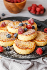Cottage cheese pancakes with raspberry and blueberry in pan on rustic background, breakfast or lunch