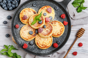 Cottage cheese pancakes with raspberry and blueberry in pan on rustic background, breakfast or lunch
