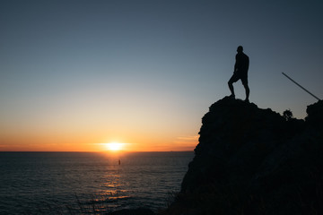 Silhouette of a guy standing on a high cliff at sunset in Galicia, Spain.