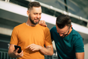 Two happy excited fan friends in euphoria mood after winning in a bet with a smartphone in hand on stadion background