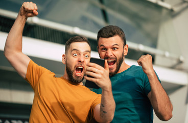 Two happy excited fan friends in euphoria mood after winning in a bet with a smartphone in hand on...