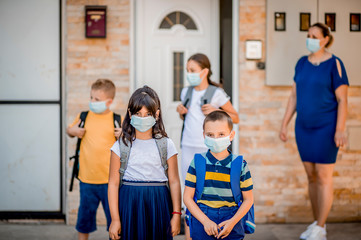 A young elementary school children are ready to go to school during the  pandemic while their mom looks on. 