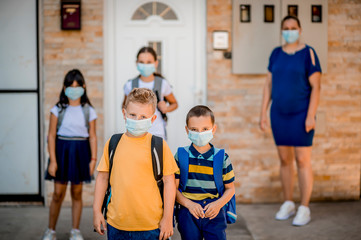 A young elementary school children are ready to go to school during the  pandemic while their mom looks on. 