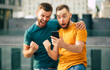 Two happy excited fan friends in euphoria mood after winning in a bet with a smartphone in hand on...