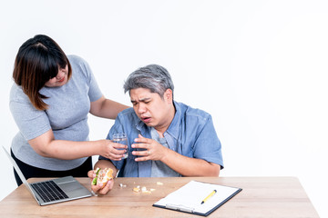 Asian attractive wife Handing a glass of water to her husband who had a throat problem, from eating a hamburger, In a hurry during work, to people and health care concept.