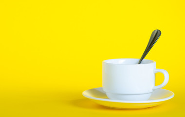 White cup with saucer teaspoon on yellow background