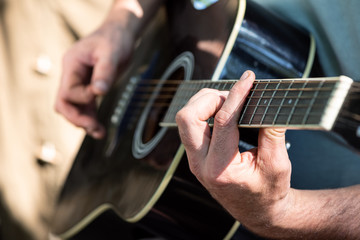 Closeup of male hands playing acoustic guitar sitting near tent outdoors. Selective focus. Romance...