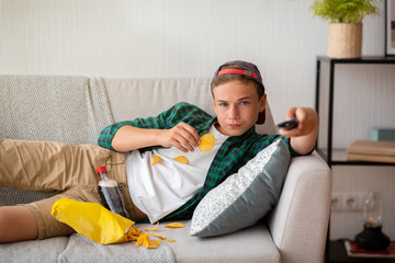 Obraz premium Teenager resting at home, watching TV and eating snacks