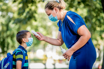 Naklejka premium Female teacher using thermometer temperature screening on children for fever against the spread virus while student is coming back to school.