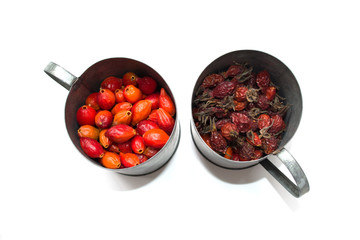 Dried rose hips in a metal mug on a white background. A scattering of berries. Close-up.