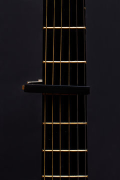 Cap on guitar fretboard on black background. Close plan. Wooden guitar.