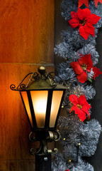 Christmas decoration with a brass lantern illuminating a stone wall and red Poinsettia flowers....