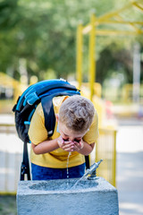Boy  drinking water from a water fountain in a park. He wearing a protective face mask down.