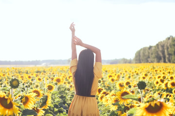 A brunette woman in a yellow dress on the field with sunflowers. Orange dress.