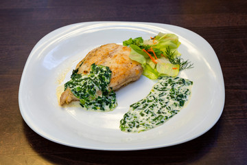 
baked chicken breast drizzled with cream sauce with herbs and salad on a white plate on a wooden surface. Healthy food. Side view
