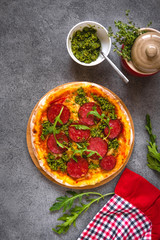 Italian pizza on dark tabletop.Traditional italian pizza with green basil pesto sauce, top view. Pepperoni pizza with Pesto.