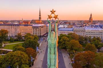 Freedom Monument surrounded by buildings and trees under the sunlight in Riga, Latvia - obrazy, fototapety, plakaty