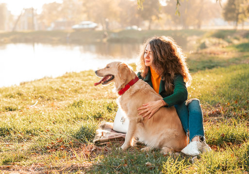 Golden retriever dog with a curly woman walking outdoors on sunny day. Training the dog in the park. love and care for the pet. Back view