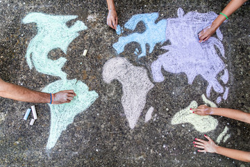 A group of people drawing with colored chalks on the floor with his hands in the street a map of...