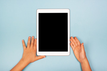 Tablet with child's hands on the blue background. The concept of digital, necessary things of a little girl, technology for children. Flat lay, copy space, isolated black display.