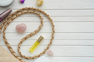 Women's flatlay with handbag, cosmetics, perfume and minerals on white wooden background.