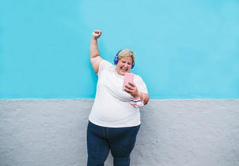 Young plus size woman with smartphone enjoy the music from playlist - Happy curvy woman dancing while wearing protective face mask - Coronavirus lifestyle