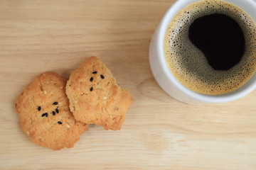 Tasty sesame cookies, one bitten piece and black coffee.