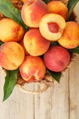 Fresh ripe peaches in a wicker basket on a wooden table, a slice of juicy peach with a stone.